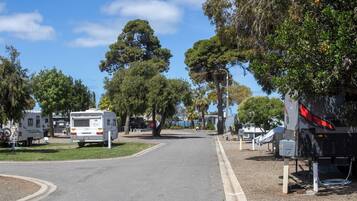 Ein Campingplatz mit Reisemobilen, die an einer befestigten Straße geparkt sind, umgeben von Bäumen und blauem Himmel.