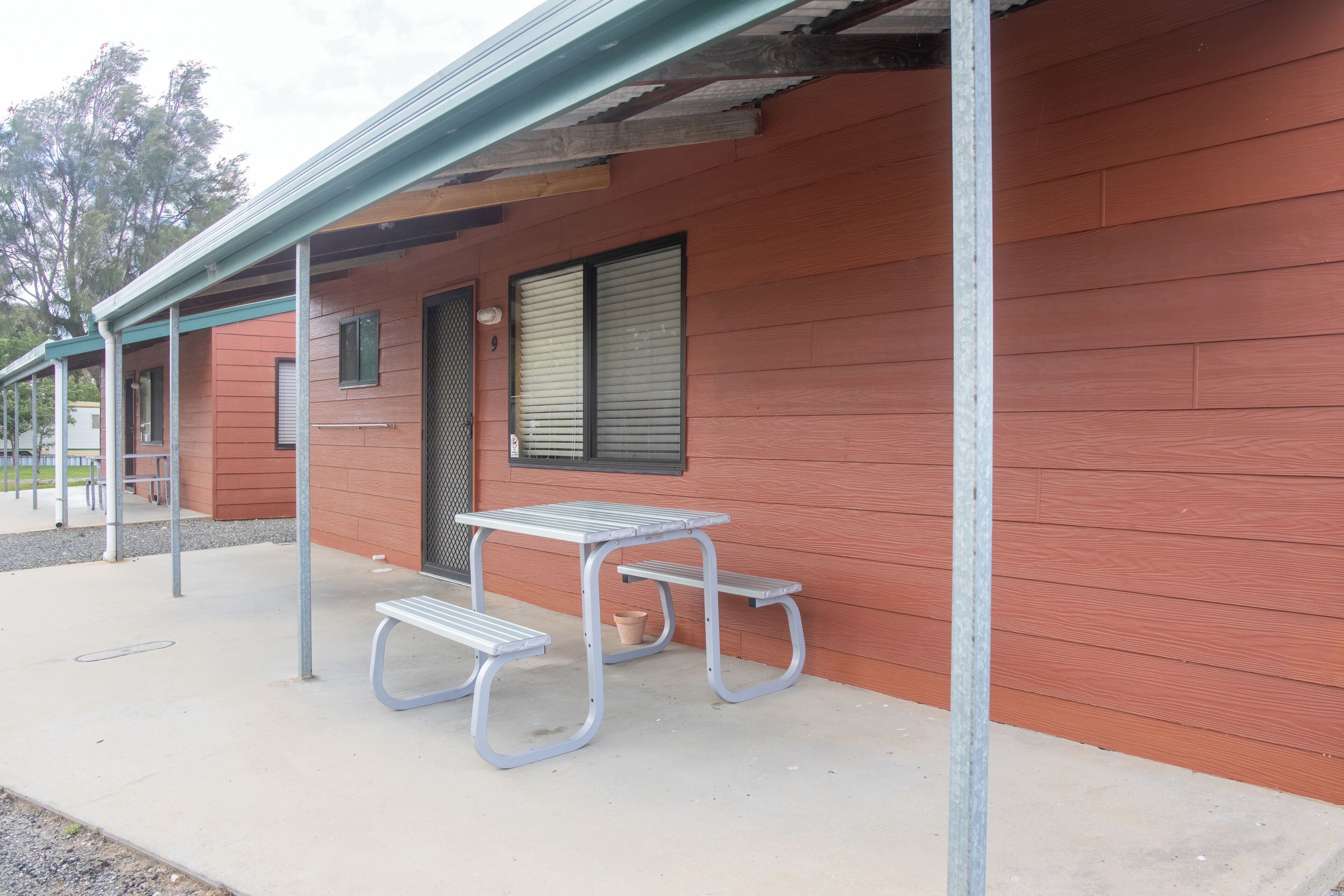 A building with a red exterior, a covered patio area with a metal table and benches, and a window with blinds.