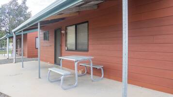 A building with a red exterior, a covered patio area with a metal table and benches, and a window with blinds.