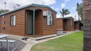 A row of small, wooden cabins with a green roof, each with a door and window, and a small patio area with a table and benches. - Tumby Bay Caravan Park (Tumby Bay)