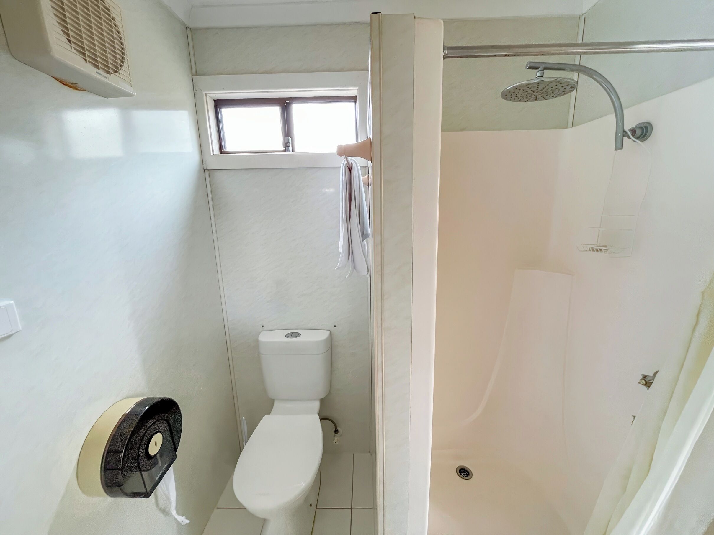 A bathroom with a toilet, a window, and a shower.
