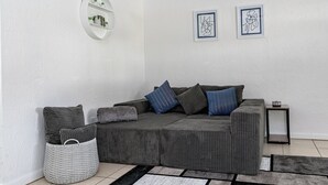 Un salon moderne avec un canapé d’angle gris, une petite table d’appoint et un panier tressé gris.