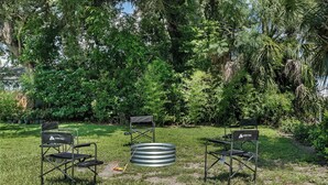 Un espace extérieur aménagé avec des chaises et une table en métal, entouré d’une végétation luxuriante et d’arbres.