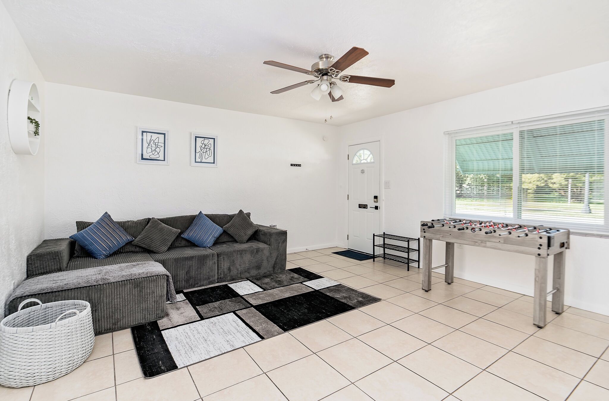 A living room with a sofa, ottoman, futsal table, and a ceiling fan.
