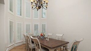 A dining room with a wooden table, six chairs, a chandelier, and white shutters on the windows. - Valley Gateaway! Pool House (Mission)