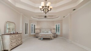 A spacious bedroom with a large bed, a dresser, a vanity, and a chandelier. - Valley Gateaway! Pool House (Mission)