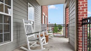 Eine Veranda mit weißen Schaukelstühlen und einem kleinen Tisch, eine Backsteinmauer und ein Metallgitter.
