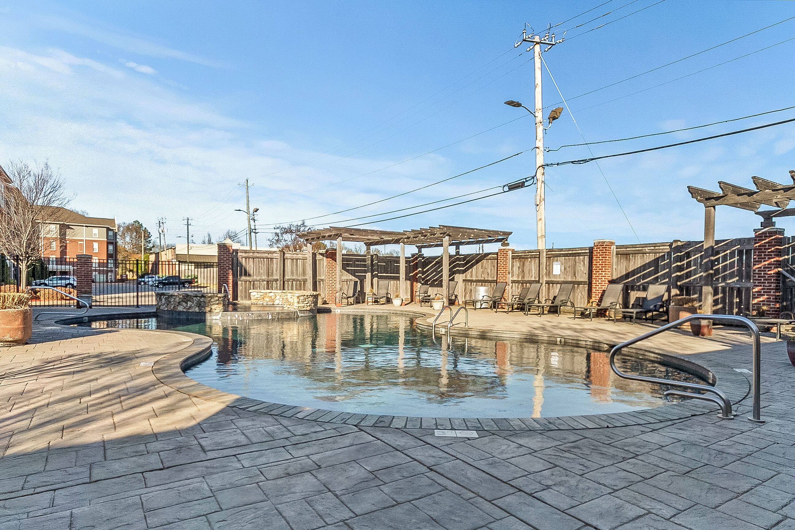 A swimming pool area with a brick deck, lounge chairs, and a pergola structure.