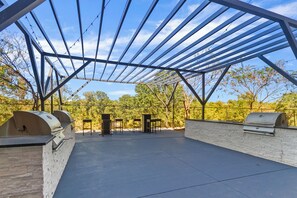 An outdoor patio with a metal roof, stone walls, and barbecue grills.