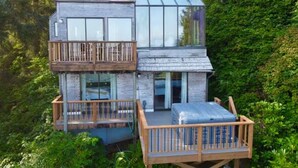 A modern two-story house with a balcony on the ground floor and a large glass window on the upper floor.
