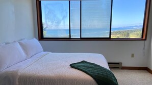 A bedroom with a large window, a bed with white linens, and a green throw blanket.
