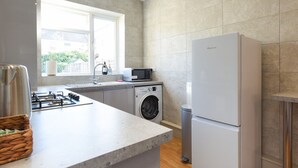 Une cuisine moderne équipée d’un lave-linge encastré, d’un réfrigérateur et d’une fenêtre laissant entrer la lumière naturelle.