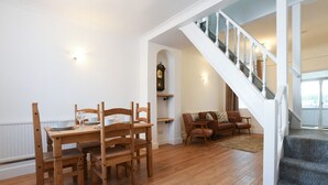 Un espace repas comprenant une table et des chaises en bois, un canapé et un escalier.