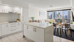 Une cuisine moderne avec des meubles blancs, un îlot central et un coin repas offrant une vue sur le panorama de la ville.