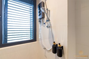 Une salle de bain avec une douche, une fenêtre avec des stores et deux bouteilles posées sur le mur.