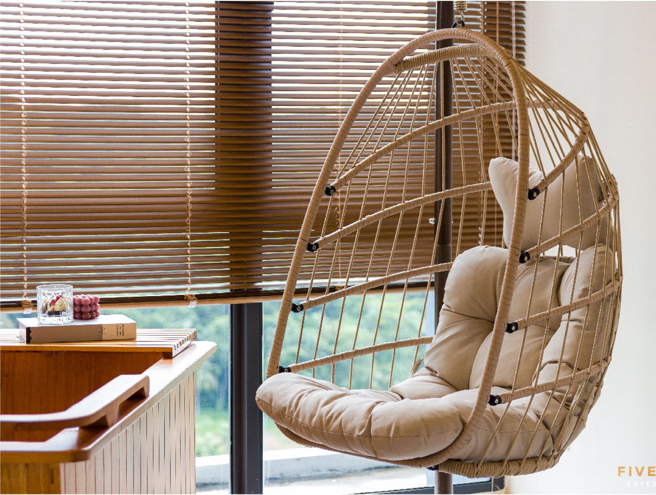A hanging chair with a cushion in a room with wooden blinds and a view of greenery outside.
