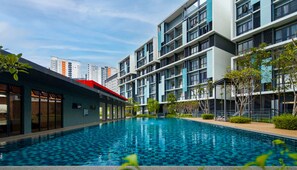 A modern hotel with a swimming pool, multiple balconies, and a view of the city skyline. - KIP Core Soho Suite by Five Senses (Sepang)