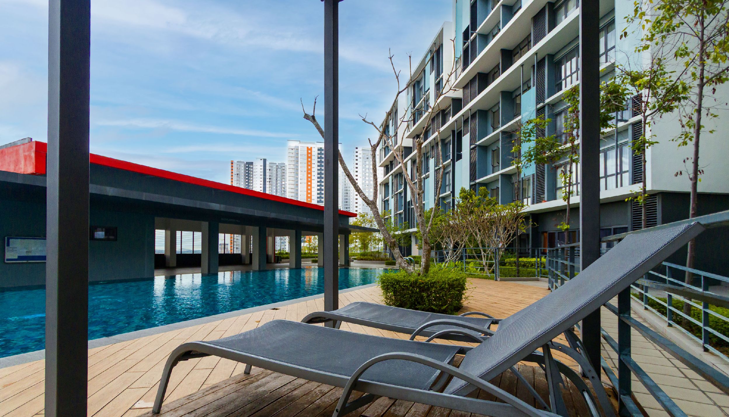 A poolside area with lounge chairs, a wooden deck, and a view of a modern building with balconies.