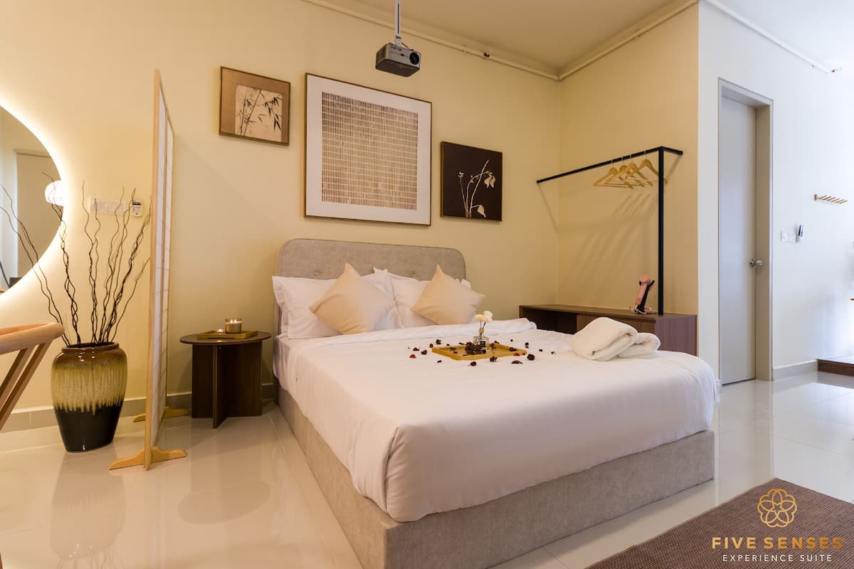 A neatly arranged bedroom with a large bed, bedside tables, a bedside lamp, and a wall-mounted projector.