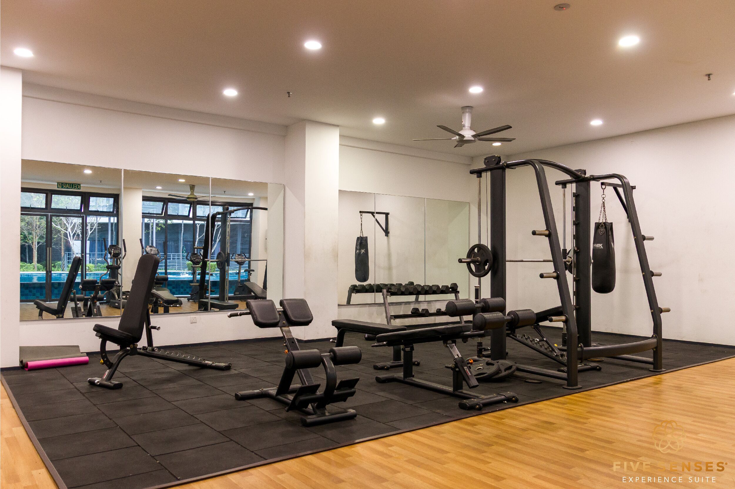 A gym with various exercise equipment, a large mirror, and windows with a view of trees.