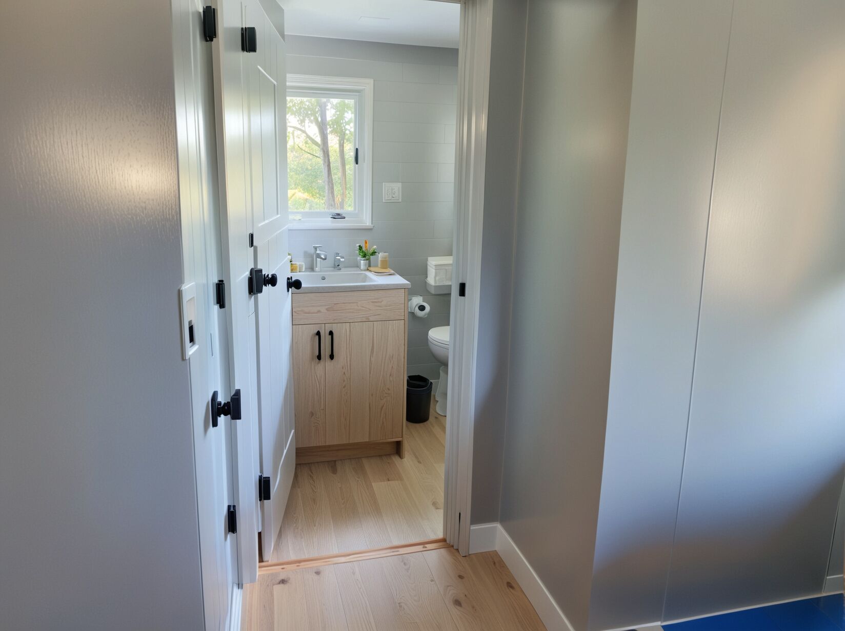 A narrow hallway leading to a bathroom with a white sink, toilet, and wooden cabinets.