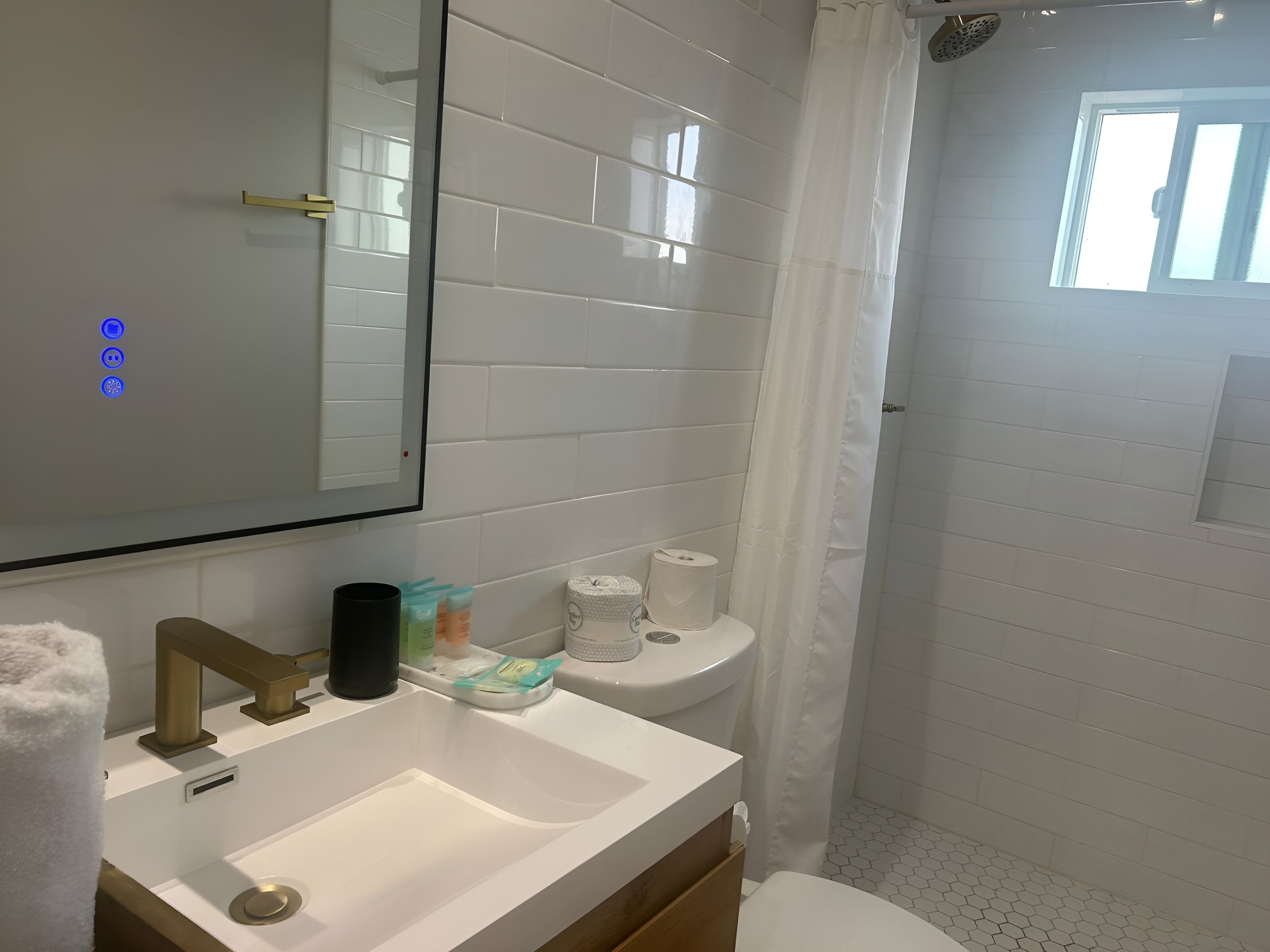 A bathroom with a white sink, mirror, and toilet. There are toiletries on the sink and a shower curtain.