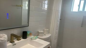 A bathroom with a white sink, mirror, and toilet. There are toiletries on the sink and a shower curtain.