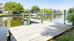 A wooden dock extending into a calm body of water, surrounded by residential houses and lush greenery.
