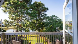 A wooden deck with wicker chairs and a table overlooking a body of water, surrounded by trees.