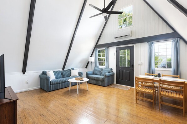 A spacious loft with a high ceiling, exposed beams, a dining area with wooden furniture, and a large window providing natural light. - The A-Frame. Canal front home in Colington Habour (Kill Devil Hills)