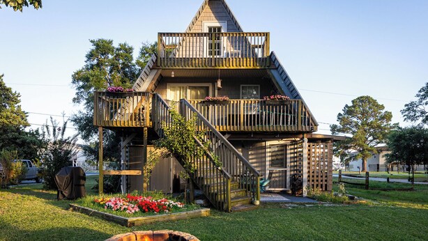 A two-story wooden house with a balcony and a fire pit in the front yard.
