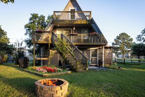 A two-story wooden house with a balcony and a fire pit in the front yard. - The A-Frame. Canal front home in Colington Habour (Kill Devil Hills)
