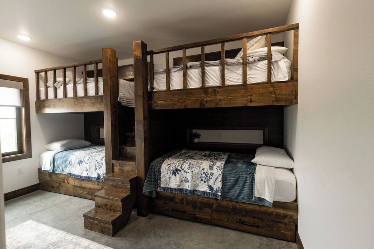 A room with two bunk beds, wooden headboards, and a small staircase.