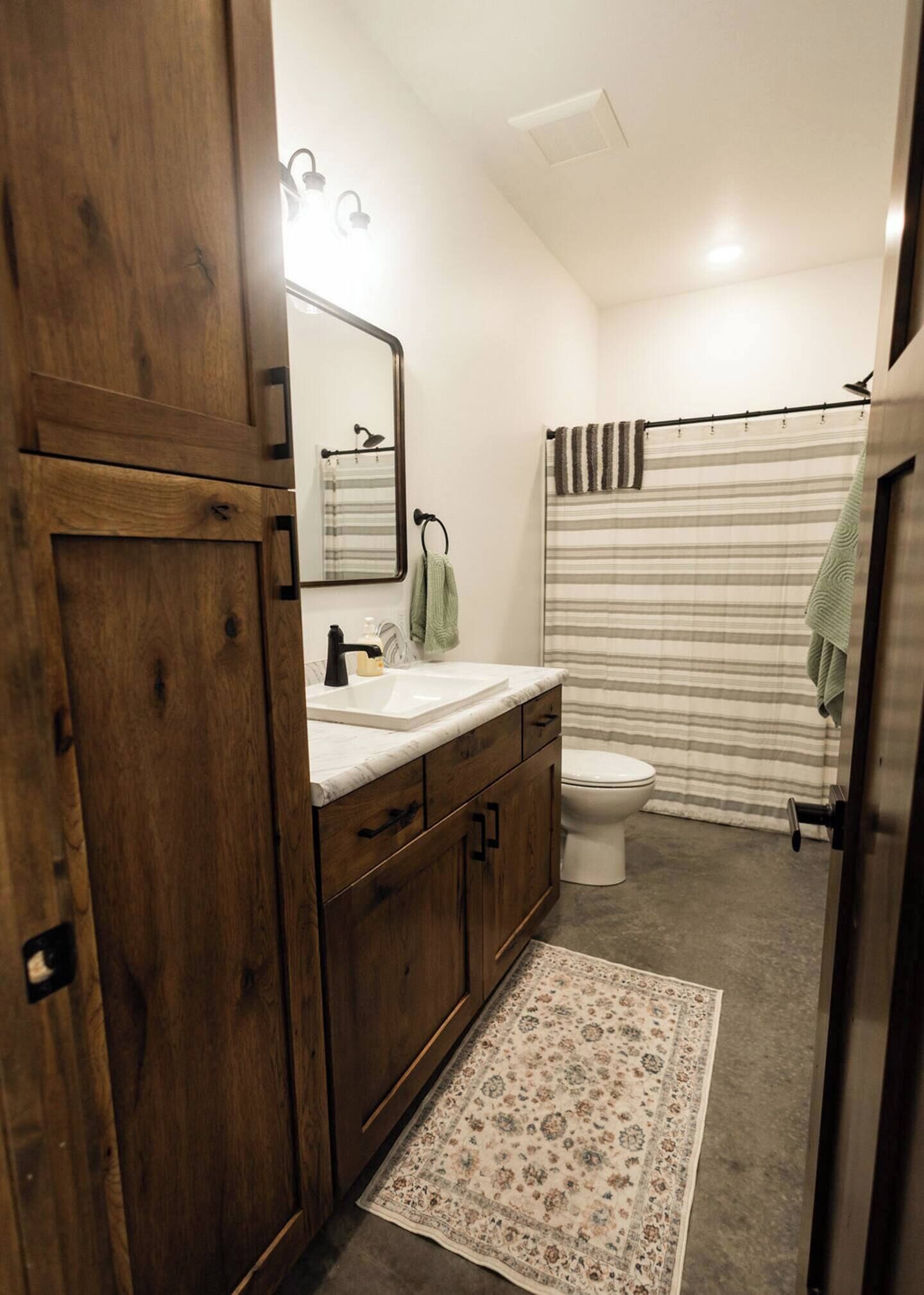 Une salle de bain avec un meuble-lavabo en bois, un évier, des toilettes et un rideau de douche.