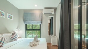 A hotel room with a bed, a window with a view of greenery, an air conditioning unit, and a mirror. - 1BR Pool Access Near Rawai Beach C222 (Rawai)