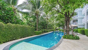 A swimming pool surrounded by lush greenery and a multi-story building. - 1BR Pool Access Near Rawai Beach C222 (Rawai)