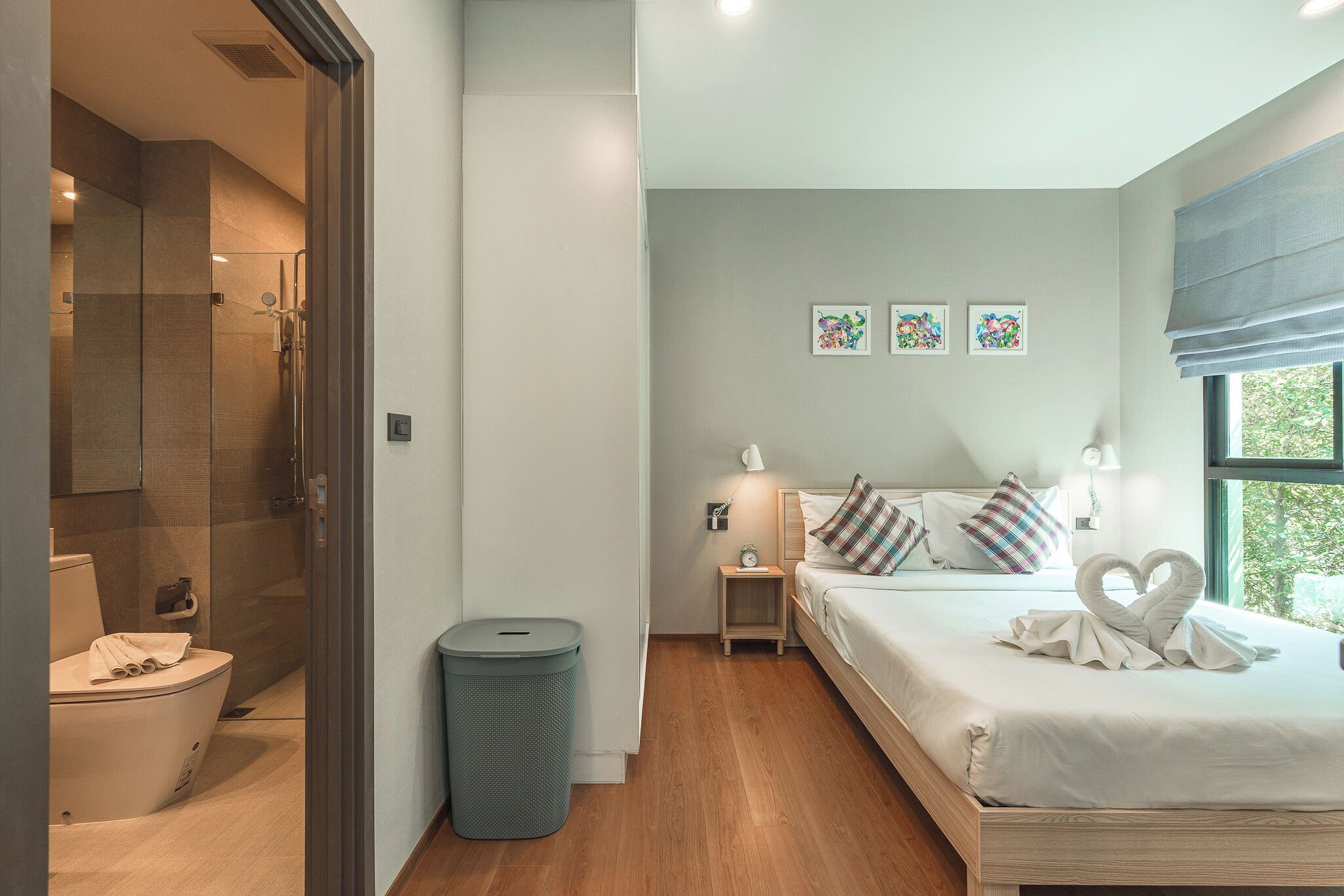 A modern hotel room with a shower, toilet, bedside table, lamp, and a bed with a heart-shaped towel decoration.