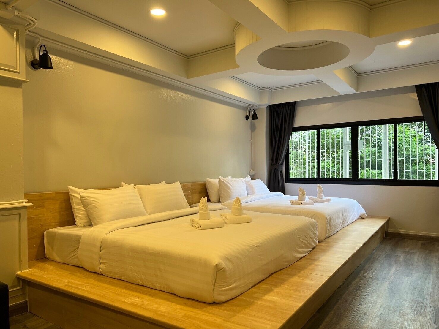 A hotel room with a large bed, a bench, a window with a view of trees, and a ceiling with recessed lighting.