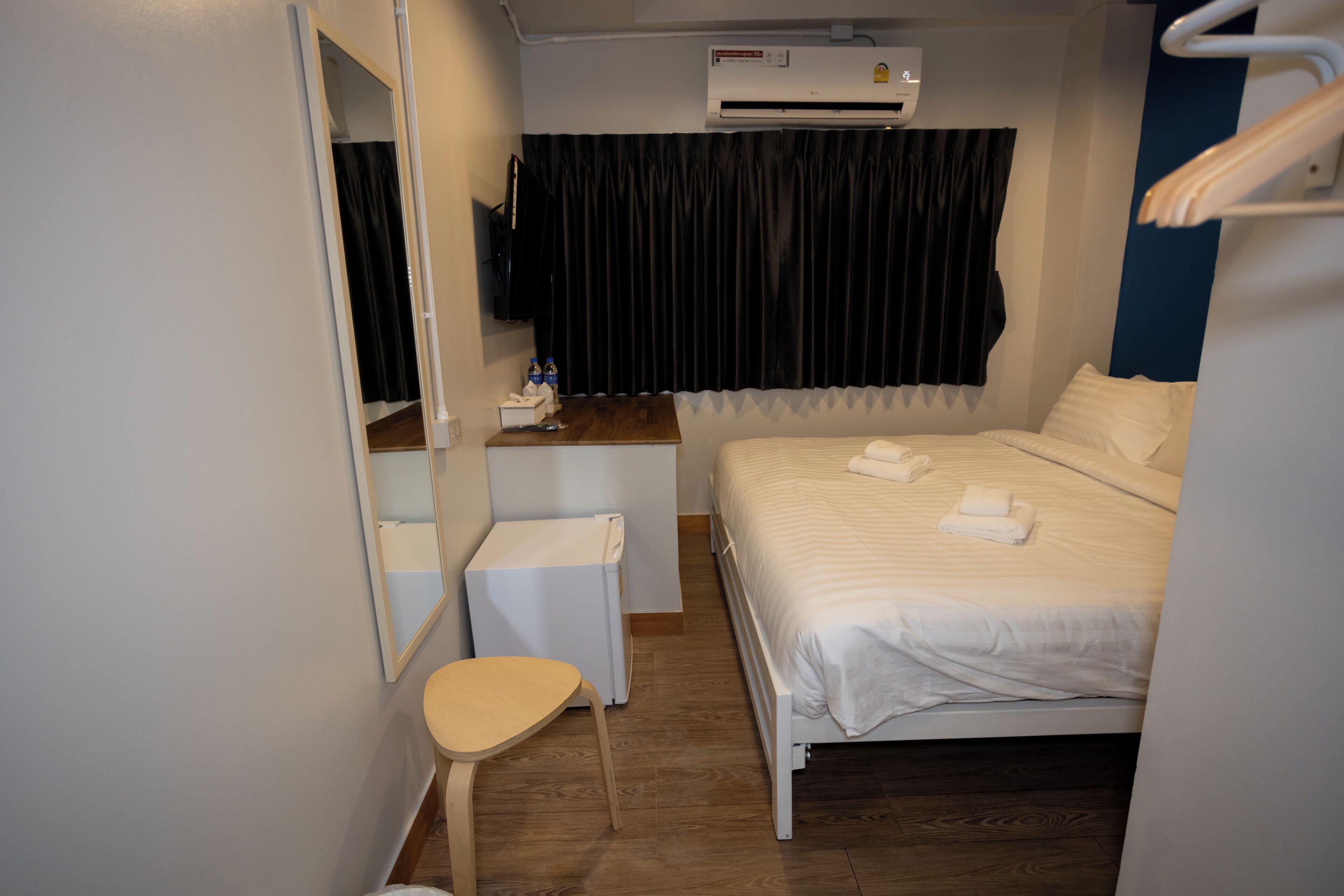 A hotel room with a bed, a desk, a chair, a mirror, a TV, and an air conditioning unit.