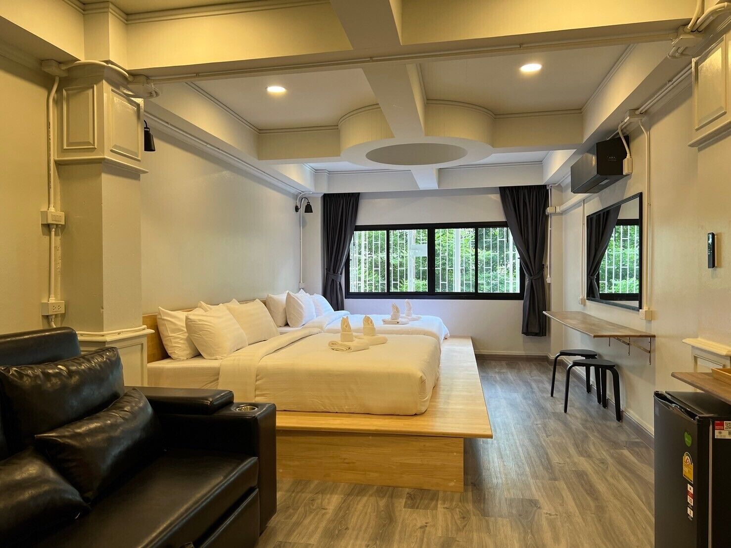 A modern hotel room with a large bed, a black leather sofa, a wooden bench, and a small table.