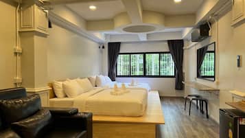 A modern hotel room with a large bed, a black leather sofa, a wooden bench, and a small table.