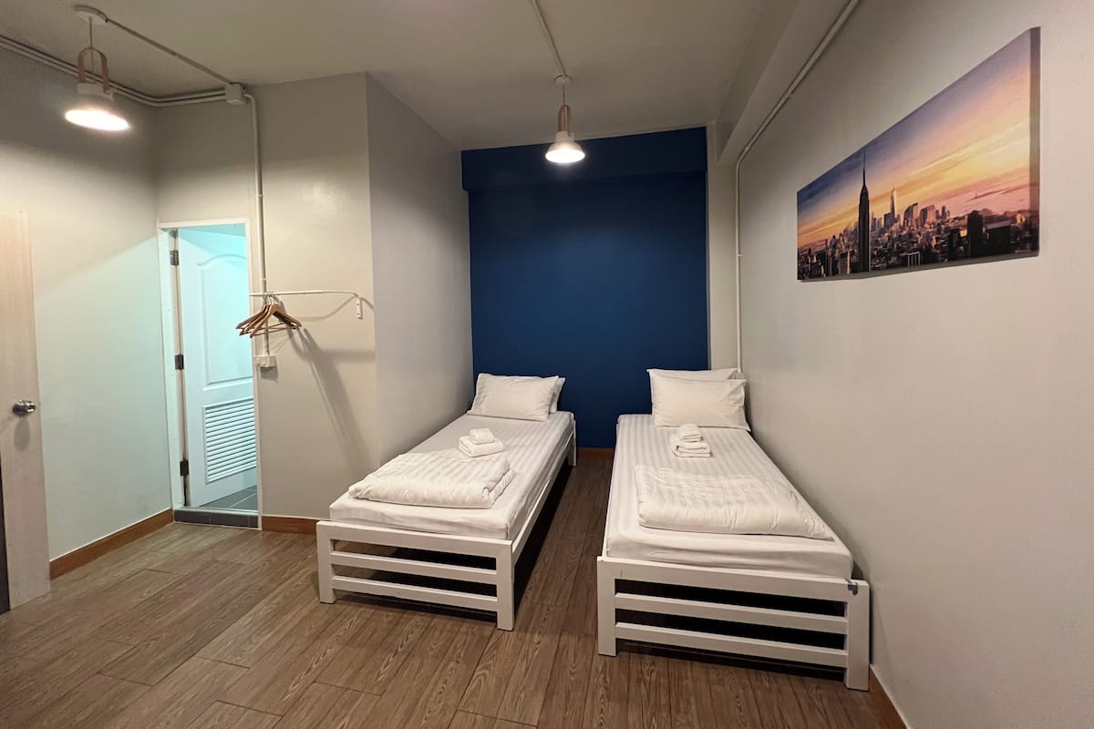Een kamer met twee eenpersoonsbedden, een deur, een kapstok en een stadsgezichtschilderij aan de muur.