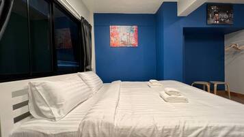 A hotel room with a bed, a window, a blue accent wall, and a painting.