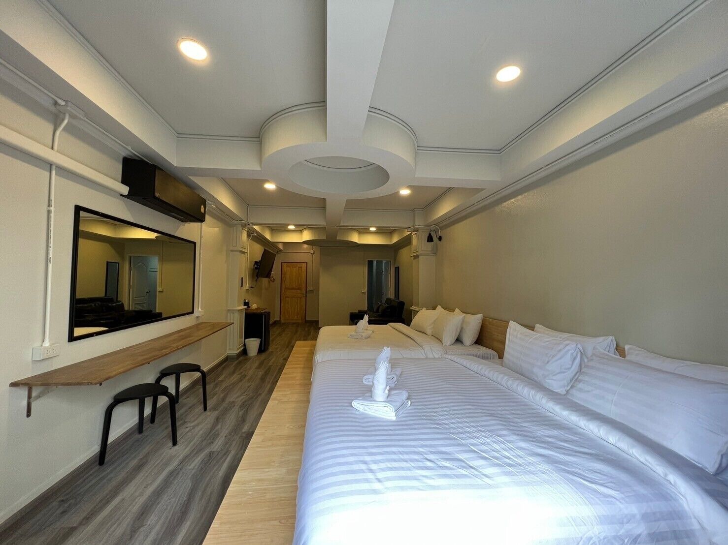 A hotel room with a large bed, a desk with a chair, a mirror, and a small seating area.