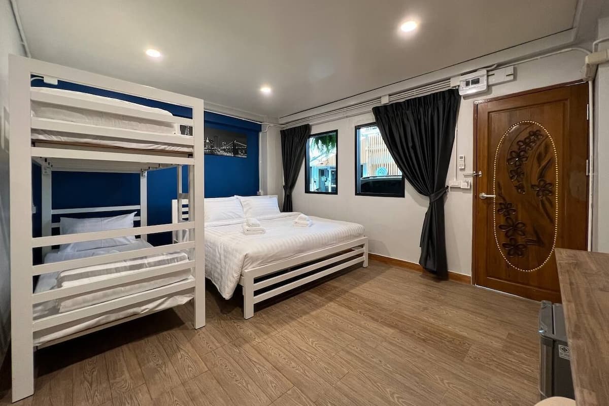Een slaapkamer met stapelbedden, een enkel bed, een houten vloer, een deur met decoratieve handgreep en een raam met gordijnen.