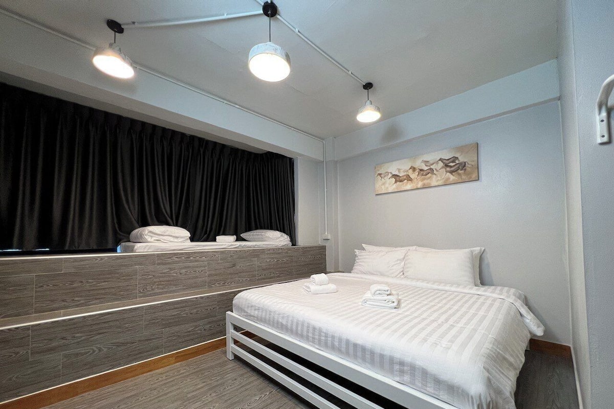Een moderne hotelkamer met een bed, een groot raam met gordijnen, een hangend kunstwerk en een ingebouwde bank aan het voeteneinde van het bed.