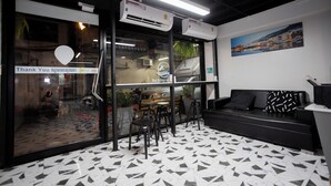 Un intérieur moderne avec un sol carrelé en noir et blanc, un canapé noir agrémenté de coussins à motifs et une grande fenêtre donnant sur l’extérieur.