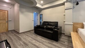 Une chambre moderne avec un canapé en cuir noir, une porte en bois et un lit doté d’une tête de lit en bois.