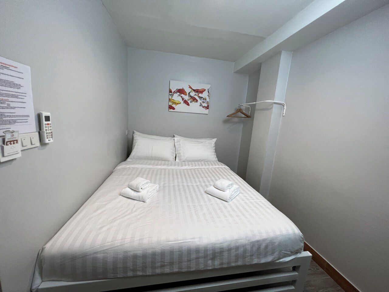A neatly made bed with white linens and towels, a small painting on the wall, and a telephone on the nightstand.