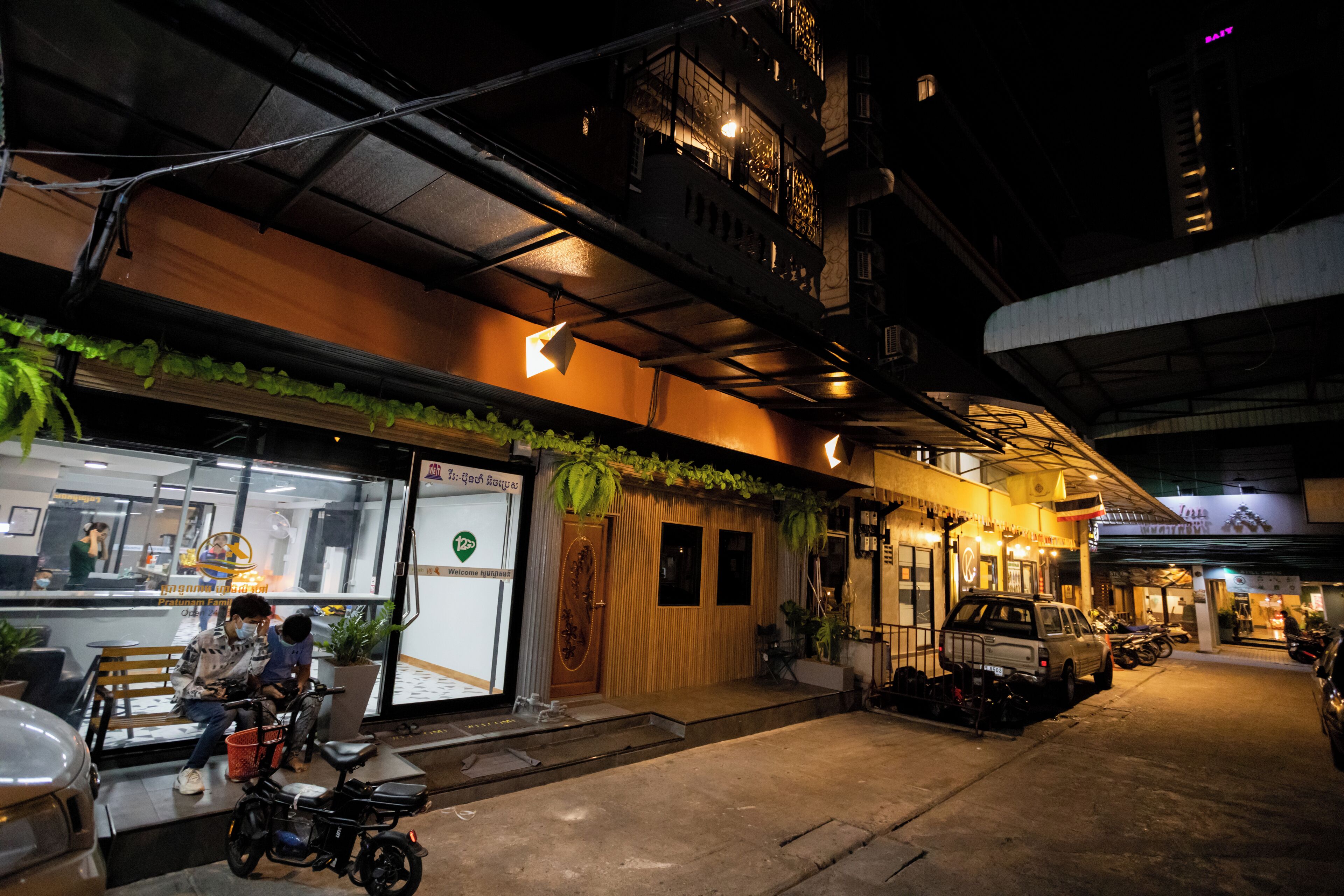 A nighttime street view with a restaurant entrance, a motorcycle, and parked cars.